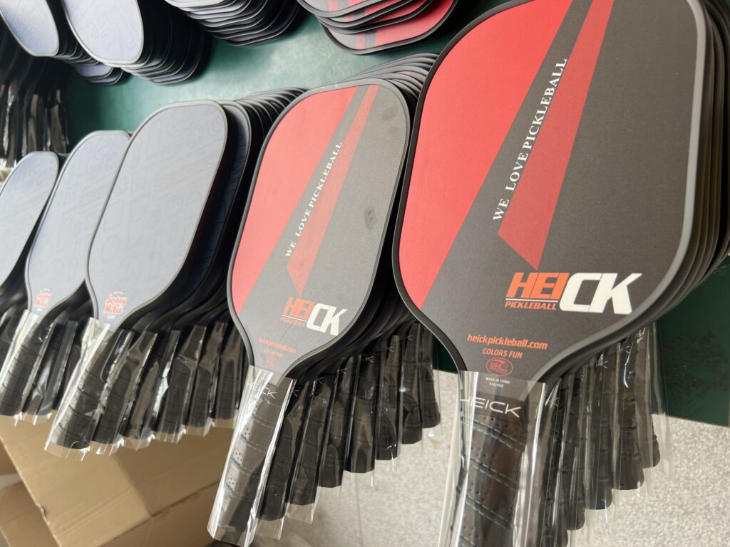 Pickleball paddle production workshop showing large batches of custom carbon fiber paddles in multiple colors, ready for assembly and packaging from a professional manufacturing factory