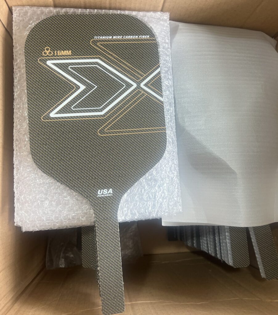 Pickleball paddle production workshop showing large batches of custom carbon fiber paddles in multiple colors, ready for assembly and packaging from a professional manufacturing factory