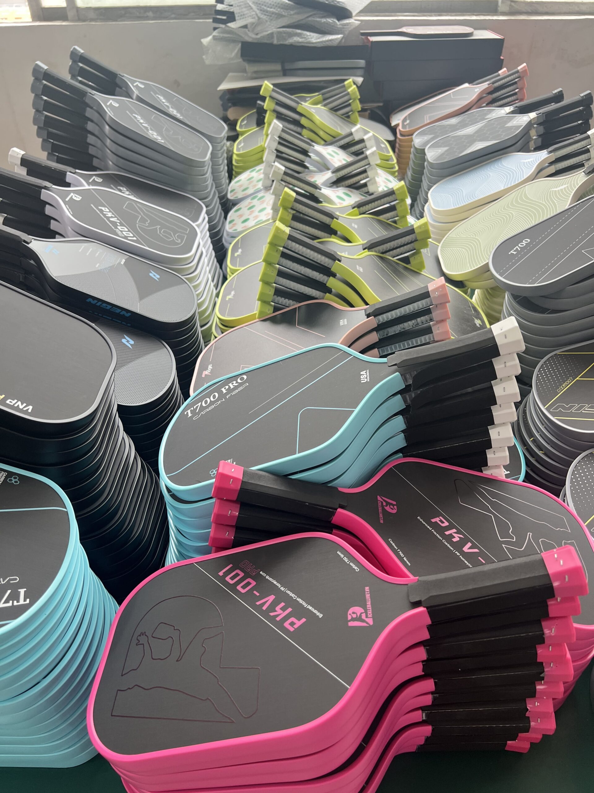 Pickleball paddle production workshop showing large batches of custom carbon fiber paddles in multiple colors, ready for assembly and packaging from a professional manufacturing factory