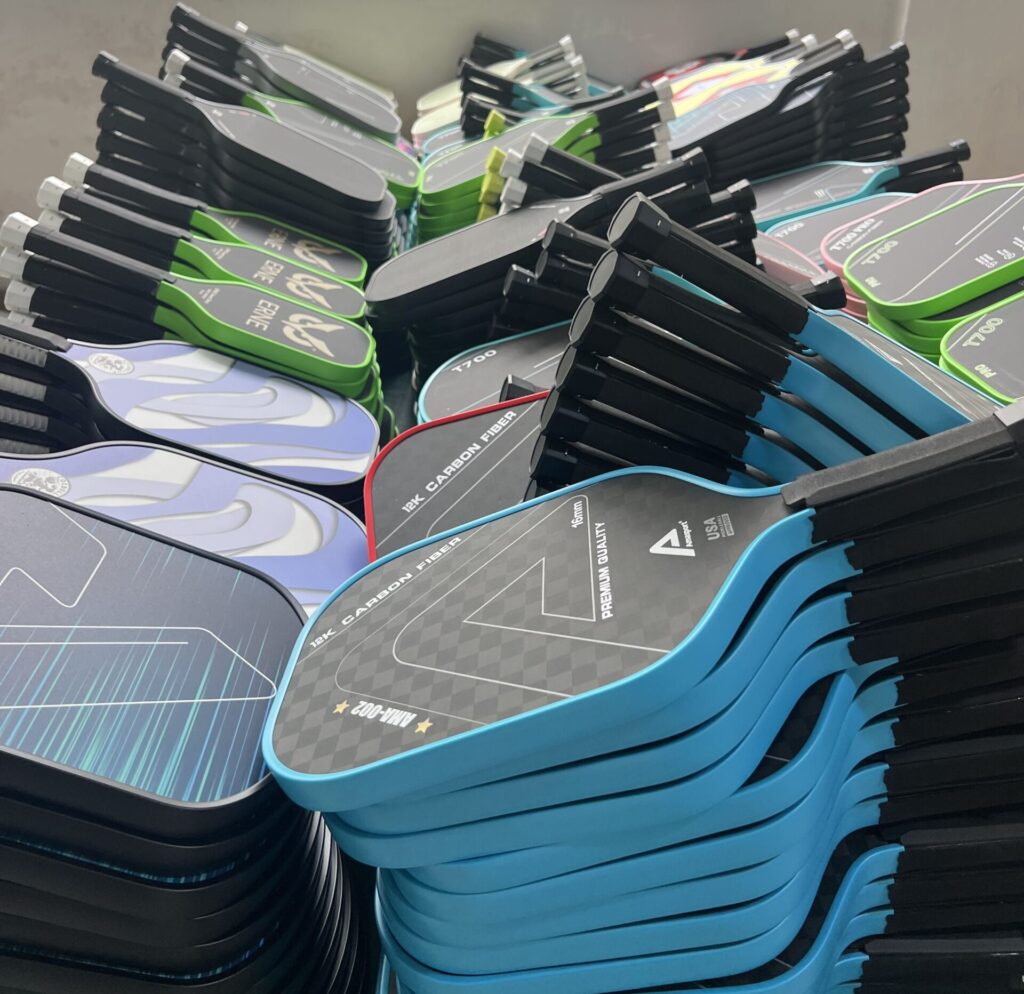 Pickleball paddle production workshop showing large batches of custom carbon fiber paddles in multiple colors, ready for assembly and packaging from a professional manufacturing factory