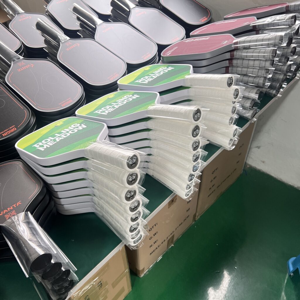 Pickleball paddle printing workshop with stacked paddle cores and workers operating printing machines for customized paddle designs