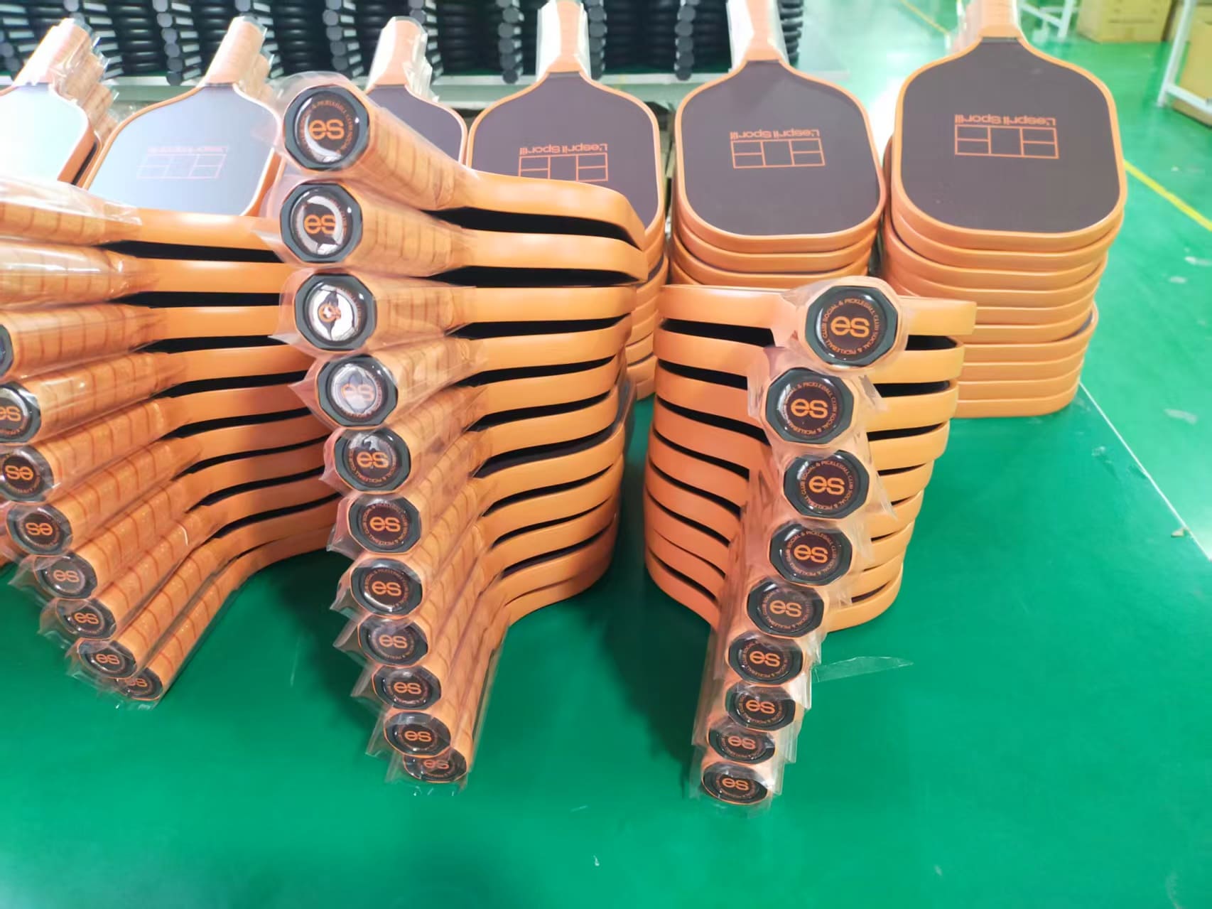 Pickleball paddle printing workshop with stacked paddle cores and workers operating printing machines for customized paddle designs